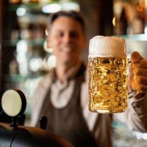 Close-up of barista holding glass of craft beer in a bar.